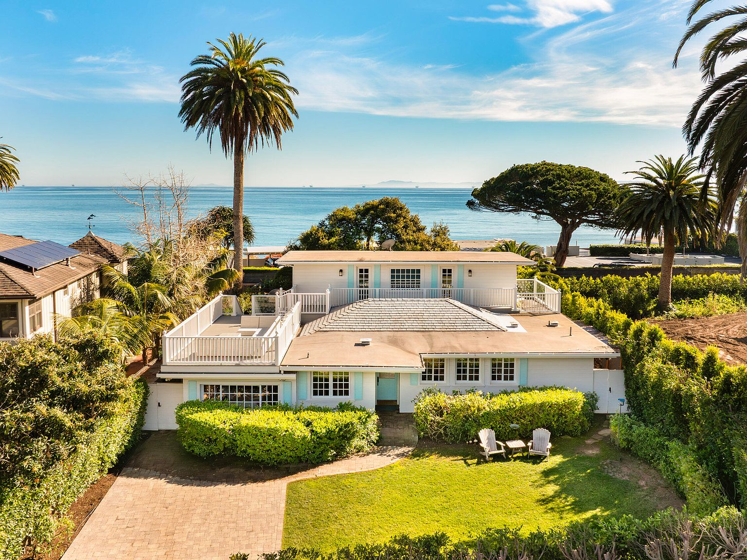 Aerial view of 22 Miramar Ave showing the white cottage nested between mature palms with the Pacific Ocean horizon beyond.